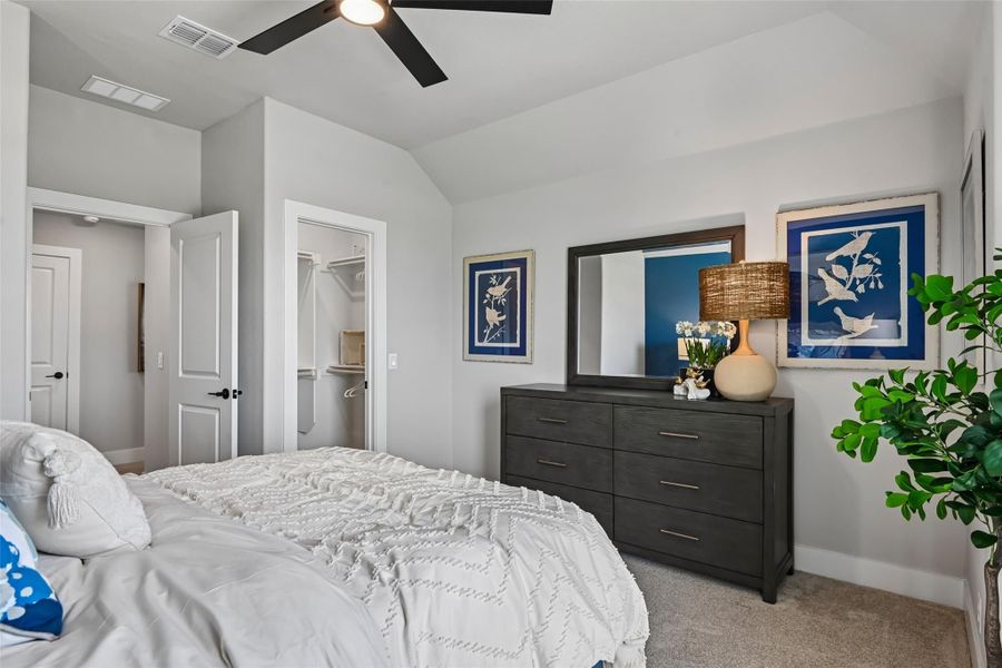 Bedroom with vaulted ceiling, ceiling fan, dark wood dresser, and walk-in closet entrance Bedroom with vaulted ceiling, ceiling fan, dark wood dresser, and walk-in closet entrance