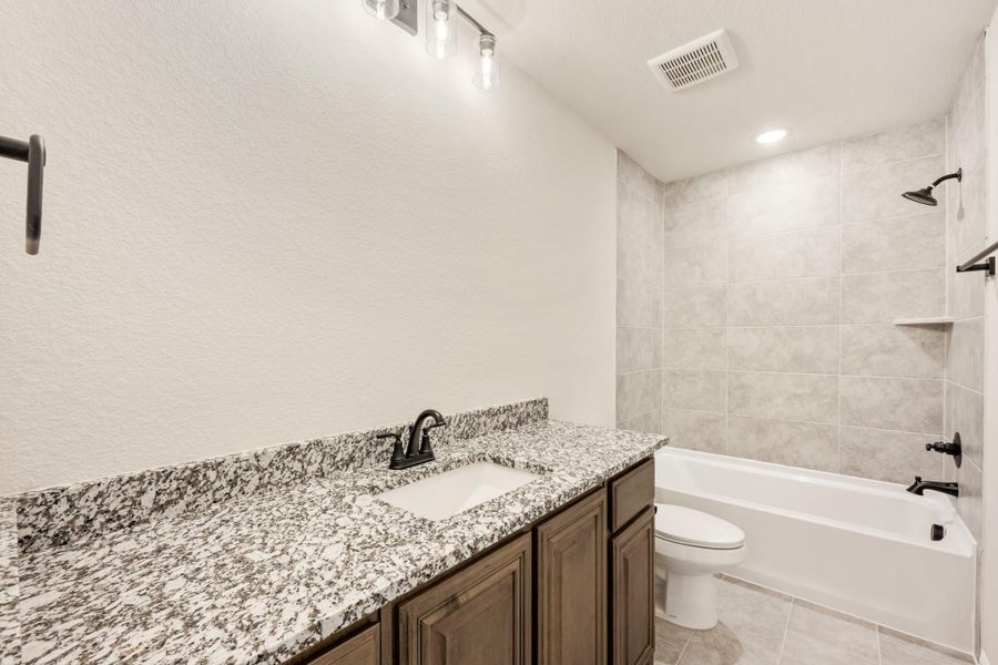 Bathroom with granite vanity, dark wood cabinets, and tiled tub-shower combo with black fixtures