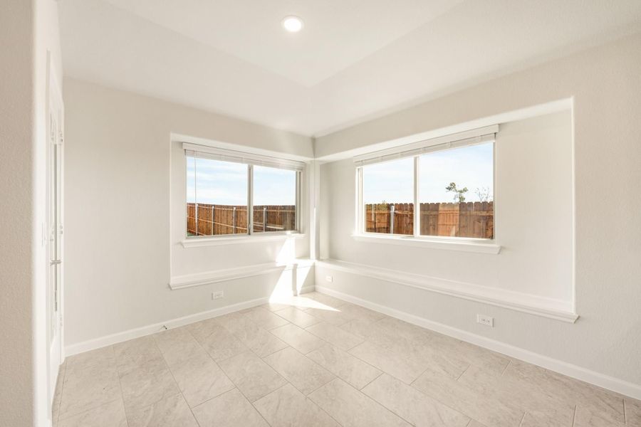 Empty room with white walls, tile floors, and two corner windows overlooking a wood fence backyard