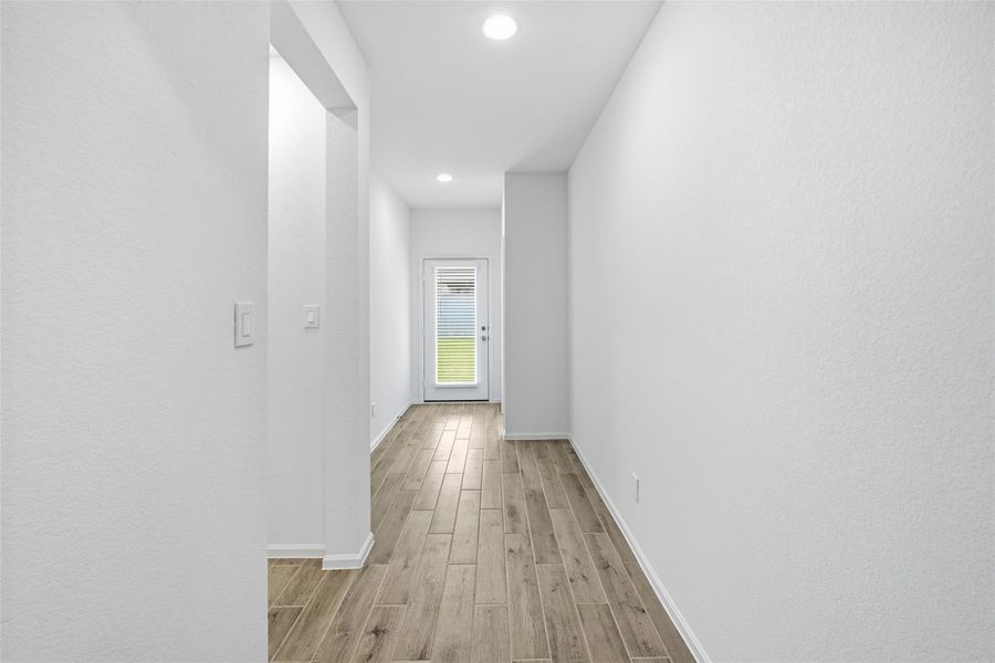 Bright, inviting hallway with sleek wood-look flooring and recessed lighting leading to a glass door.