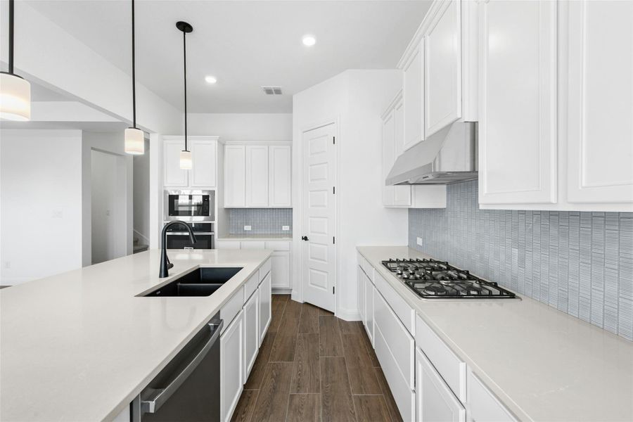 Kitchen with wood finish floors, white cabinetry, pendant lighting, stainless steel appliances, and decorative backsplash