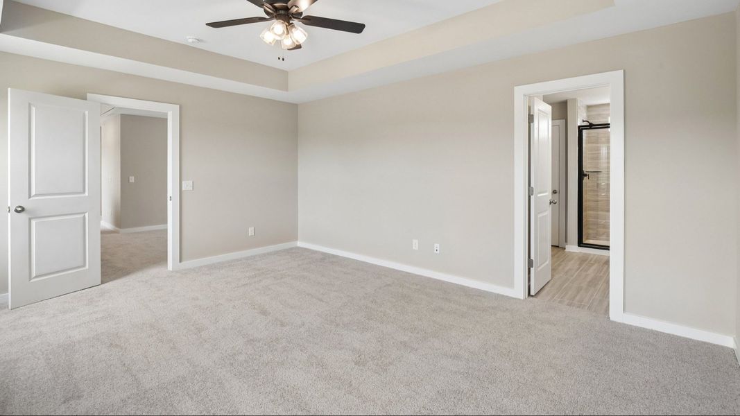 Bedroom with tray ceiling, ceiling fan, and entrance to primary bathroom