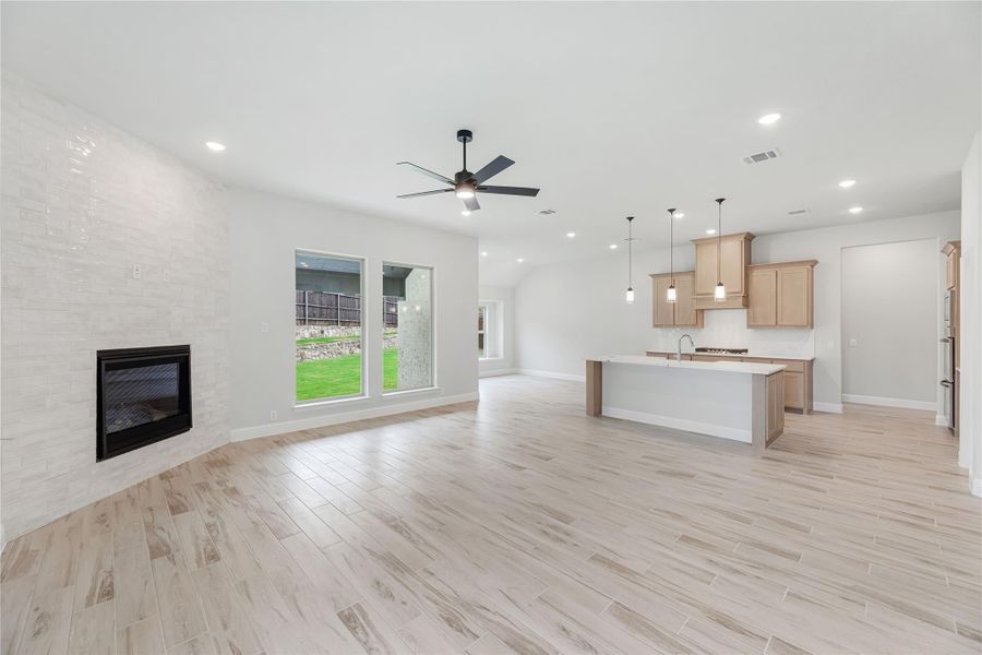 Open-concept living area with tile fireplace, ceiling fan, and kitchen island with light wood cabinets and pendant lights Open-concept living area with tile fireplace, ceiling fan, and kitchen island with light wood cabinets and pendant lights