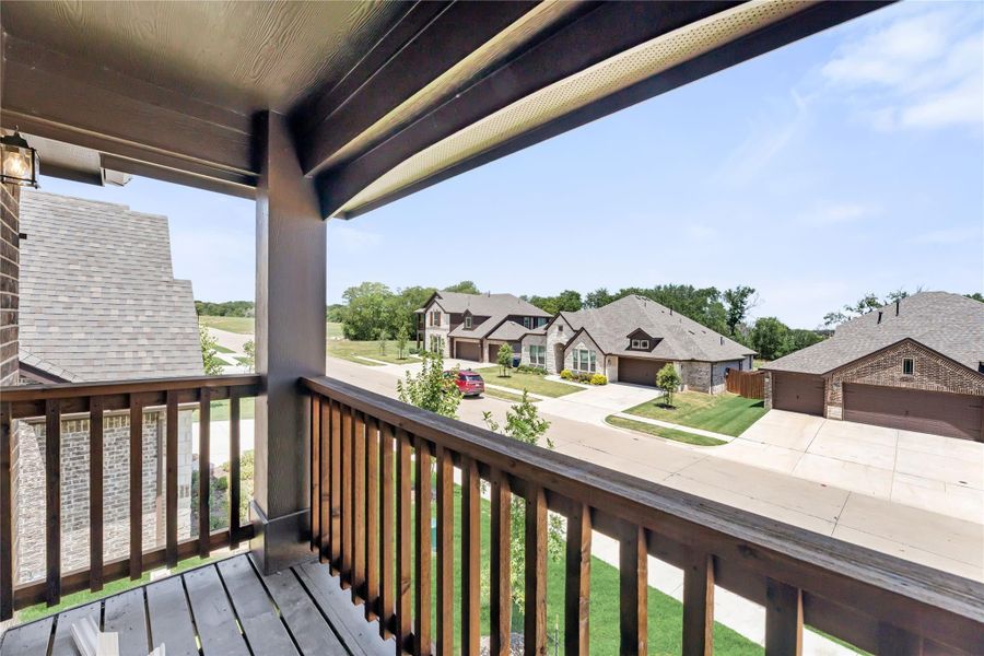 Covered second-floor balcony with wood railing overlooking a residential neighborhood street with brick homes