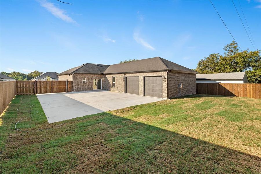 Back of house featuring a fenced backyard, brick siding, roof with shingles, concrete driveway, and an attached garage