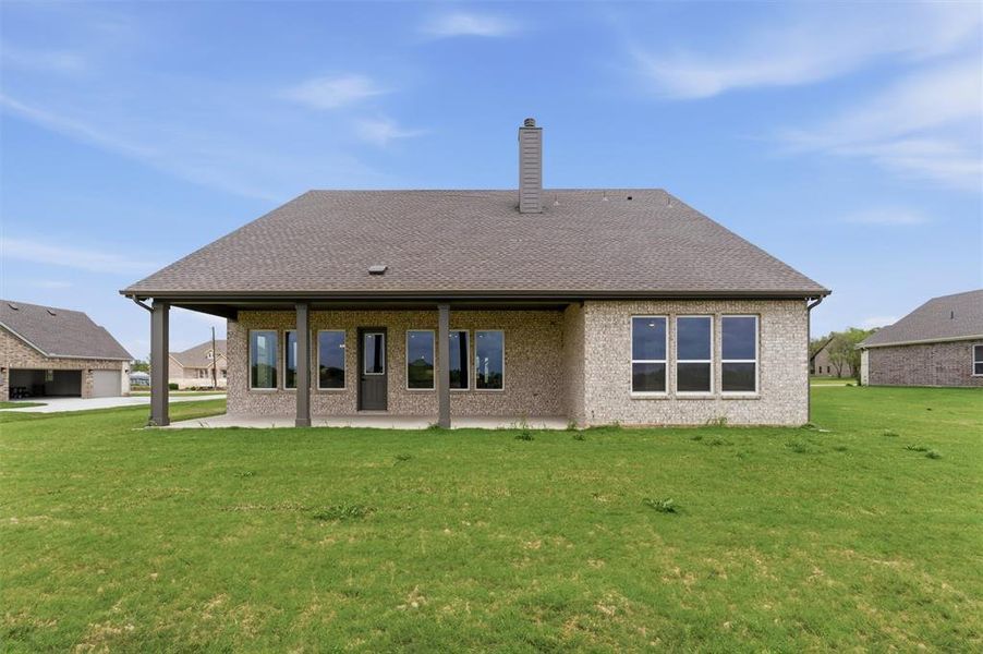 Rear view of house with a lawn, a patio area, a chimney, brick siding, and roof with shingles
