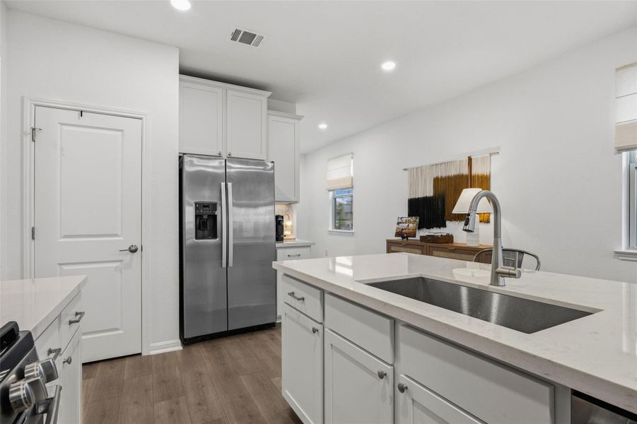 Kitchen featuring white cabinetry with brushed nickel hardware, stainless steel side-by-side refrigerator, wood-finish flooring, recessed lighting, and a kitchen island with an undermount sink and gooseneck faucet