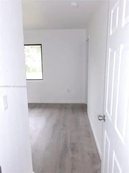 Interior space featuring wood-finish flooring, white walls, and a multi-panel door with a metallic hardware finish