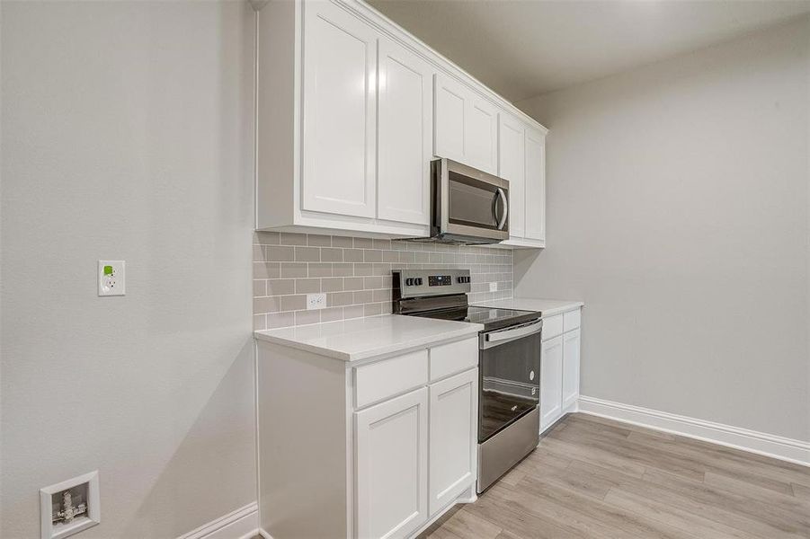Kitchen featuring stainless steel appliances, decorative backsplash, light countertops, white cabinetry, and light wood-style flooring Kitchen featuring stainless steel appliances, decorative backsplash, light countertops, white cabinetry, and light wood-style flooring
