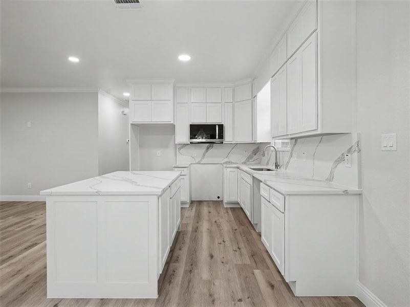 Modern kitchen featuring white cabinetry, quartz countertops with integrated backsplash, a center island, recessed lighting, and wood-finish flooring