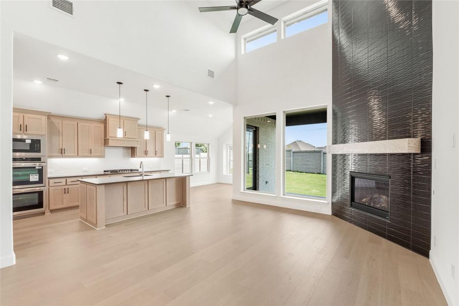 Open living area with vaulted ceiling, kitchen island, hardwood floors, and floor-to-ceiling tiled fireplace