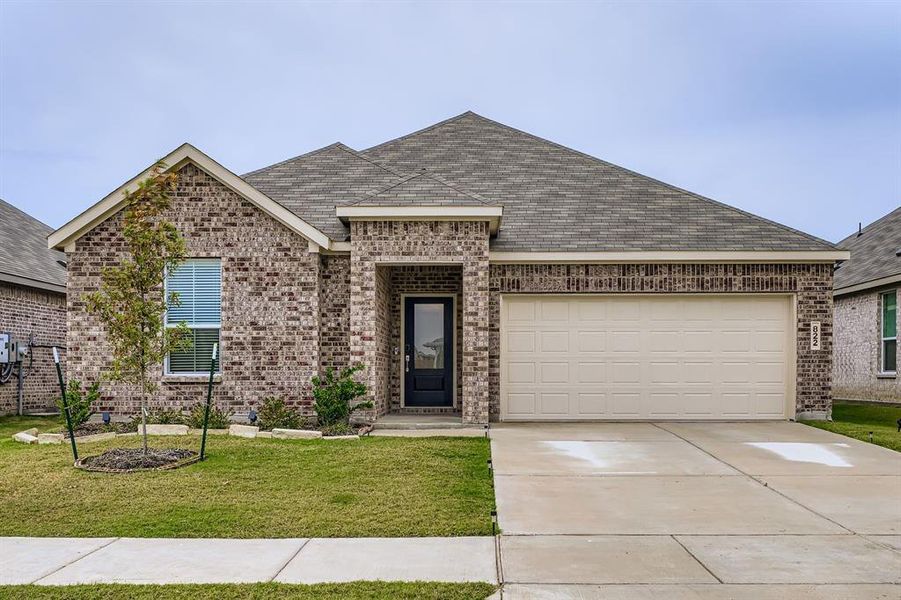 Ranch-style house with a shingled roof, driveway, a front yard, and brick siding