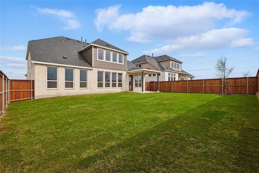 Rear view of property with a fenced backyard, a shingled roof, brick siding, and a yard