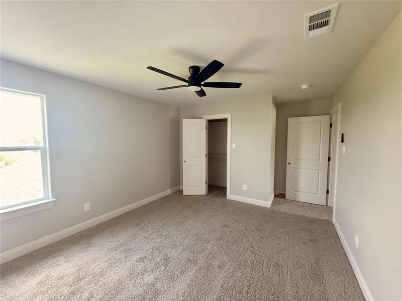 Spacious room featuring neutral carpeting, light-toned walls, and a ceiling fan with dark blades