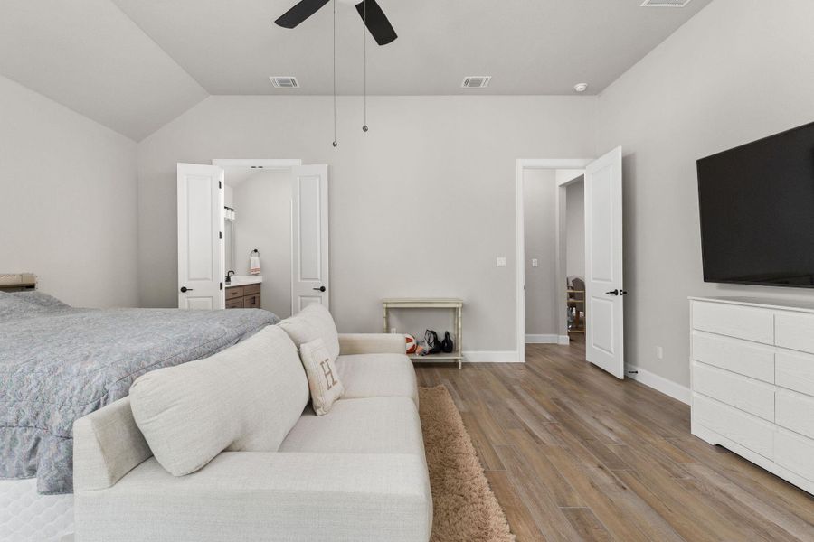 Bedroom featuring wood finished floors, a ceiling fan, vaulted ceiling, and ensuite bath