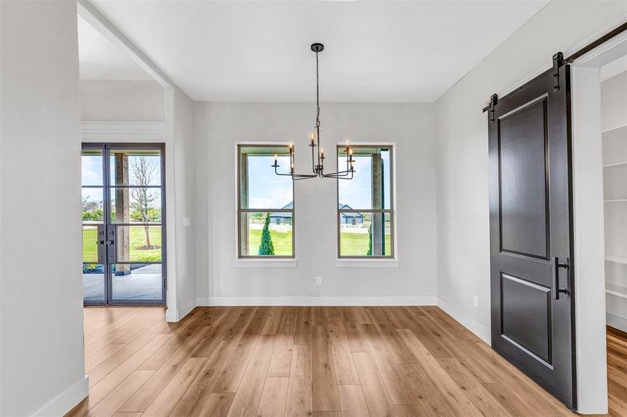 Unfurnished dining area with a barn door, a chandelier, and light hardwood / wood-style floors