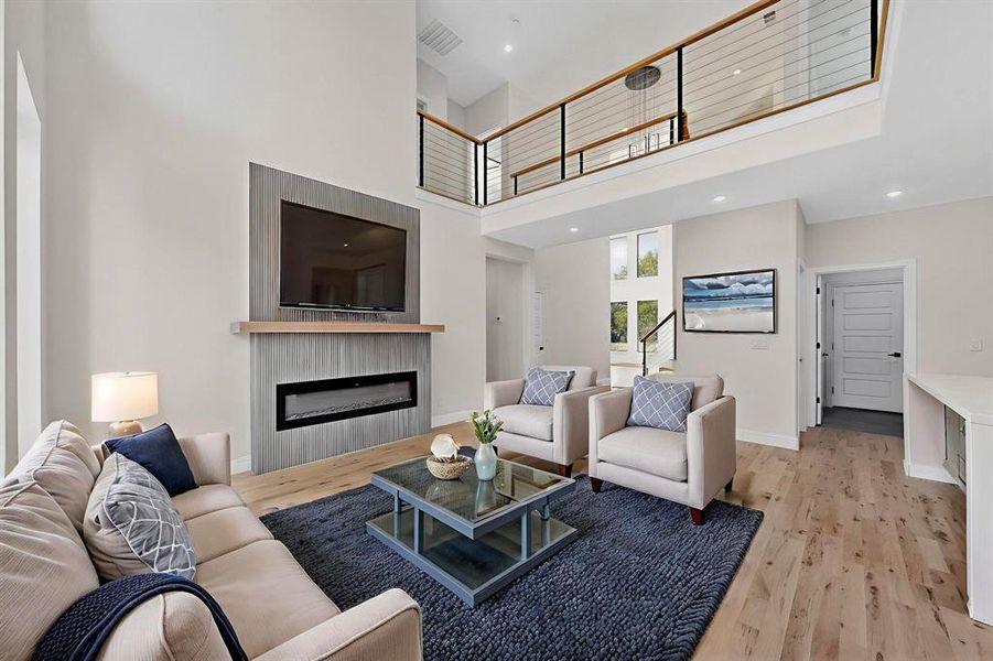 Living area featuring light wood-style floors, a towering ceiling, a glass covered fireplace, and recessed lighting Living area featuring light wood-style floors, a towering ceiling, a glass covered fireplace, and recessed lighting
