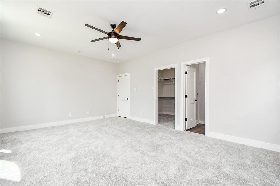 This is a spacious, well-lit Master ensuite room with neutral walls and carpeting, featuring a modern ceiling fan and recessed lighting. The room includes a large walk in closet with built-in shelves, providing ample storage space.