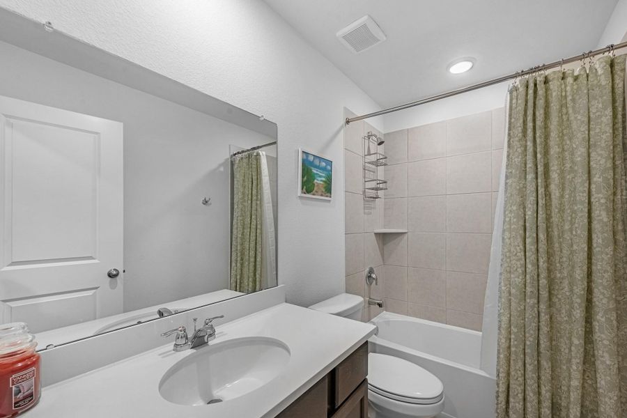 The secondary bath features tile flooring, custom stained cabinetry and light countertops and a shower/tub combo. Perfect for accommodating any visiting family and friends.