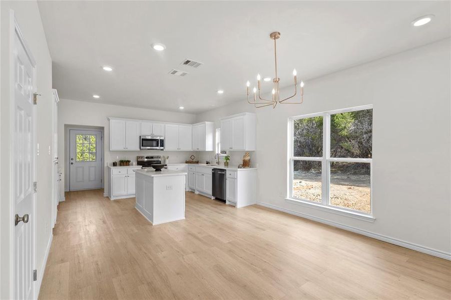 Kitchen with light countertops, white cabinetry, a center island, recessed lighting, and hanging light fixtures Kitchen with light countertops, white cabinetry, a center island, recessed lighting, and hanging light fixtures