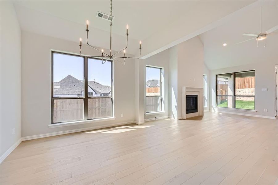 Unfurnished living room with high vaulted ceiling, light wood-type flooring, and ceiling fan with notable chandelier