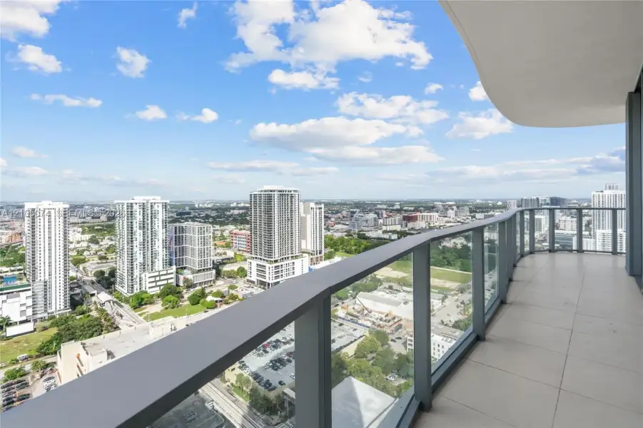 Covered balcony featuring expansive tile flooring and a glass railing system with a metal frame