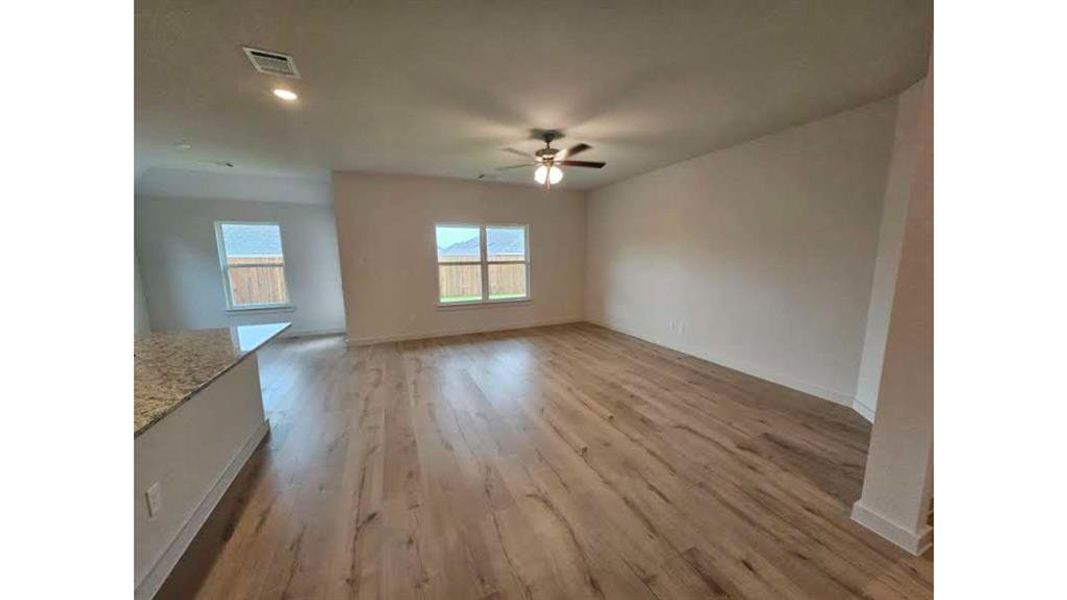 Spacious living area featuring wood-finish flooring, ample natural light from multiple windows, recessed lighting, and a ceiling fan
