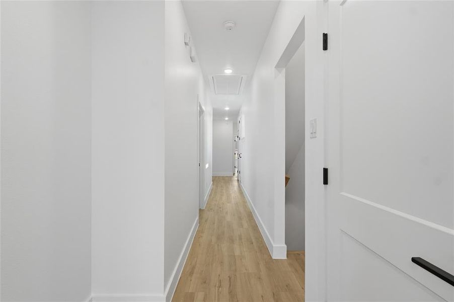 Hallway with light wood finished floors, an upstairs landing, and recessed lighting