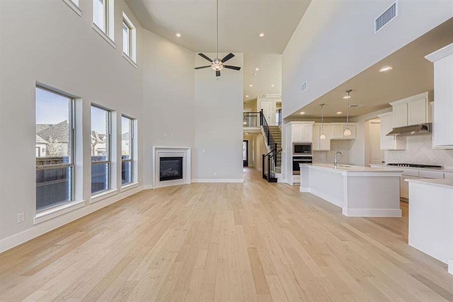 Unfurnished living room with ceiling fan, a glass covered fireplace, light wood-style flooring, a towering ceiling, and stairway