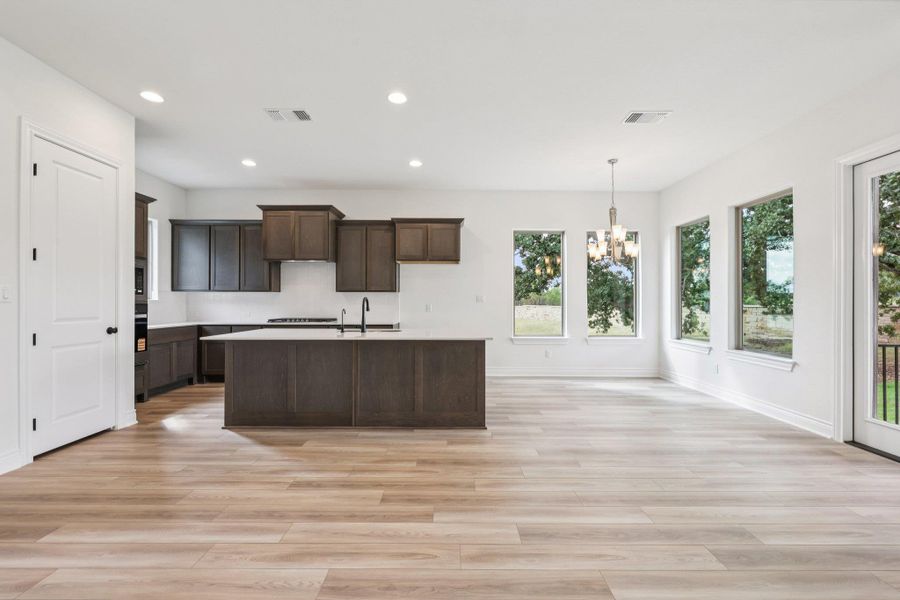 Kitchen with recessed lighting, light wood finished floors, a kitchen island with sink, pendant lighting, and a chandelier