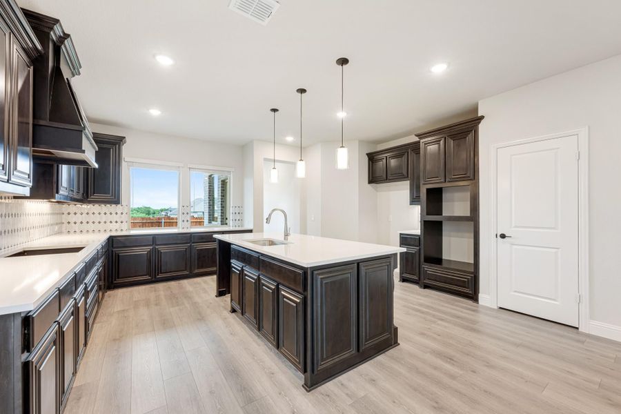 Kitchen with dark wood cabinets, center island with sink, pendant lights, and light hardwood floors