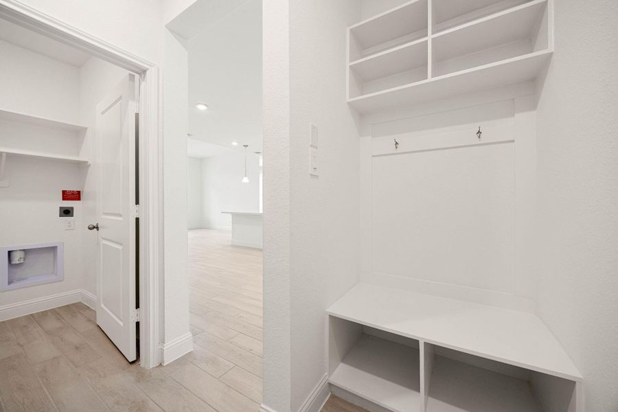 A bright and spacious mudroom with built-in storage and hooks offers convenience and organization, leading into a light-filled area with modern flooring.
