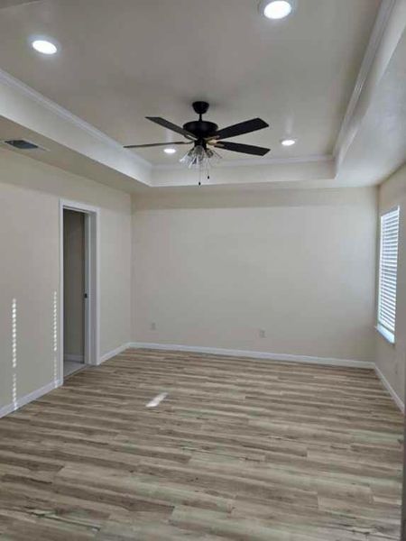 Empty room with a ceiling fan, light wood-style floors, crown molding, recessed lighting, and a tray ceiling Empty room with a ceiling fan, light wood-style floors, crown molding, recessed lighting, and a tray ceiling