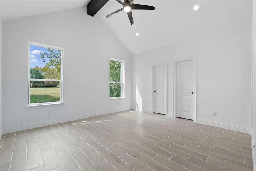 Unfurnished bedroom with high vaulted ceiling, beam ceiling, wood finish floors, ceiling fan, and two closets Unfurnished bedroom with high vaulted ceiling, beam ceiling, wood finish floors, ceiling fan, and two closets