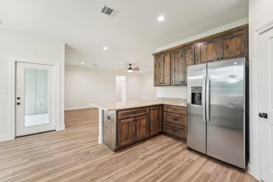 Kitchen featuring a peninsula,Vinyl Wood Plank floor, visible vents, light stone countertops, and stainless steel refrigerator with ice dispenser Kitchen featuring a peninsula,Vinyl Wood Plank floor, visible vents, light stone countertops, and stainless steel refrigerator with ice dispenser