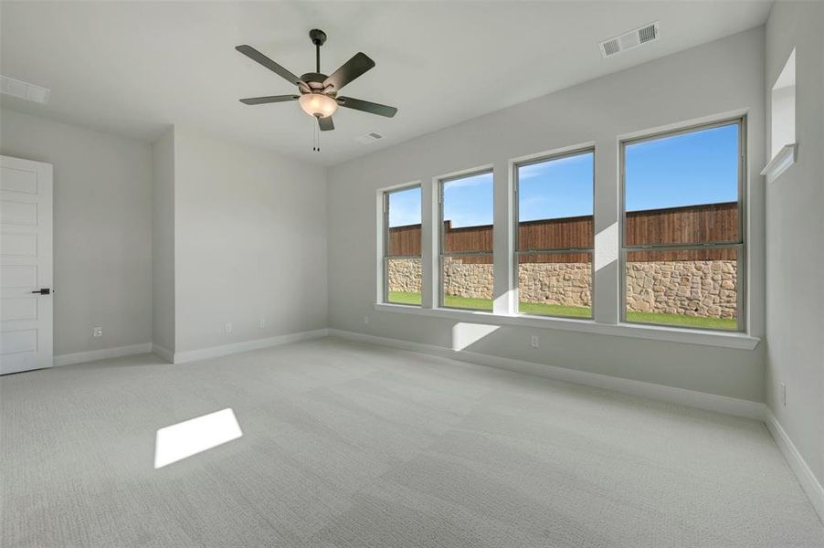 Spacious room featuring light gray carpeting, a multi-paneled door with dark hardware, and a ceiling fan with integrated lighting