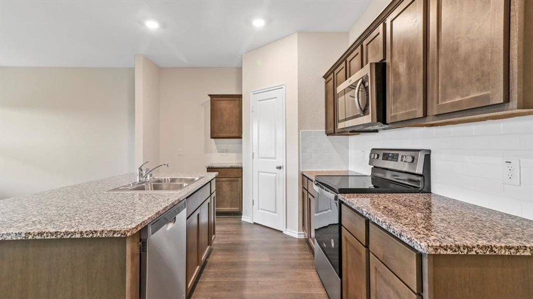 Kitchen featuring wood-finish flooring, granite countertops, and stainless steel appliances including a range, microwave, and dishwasher