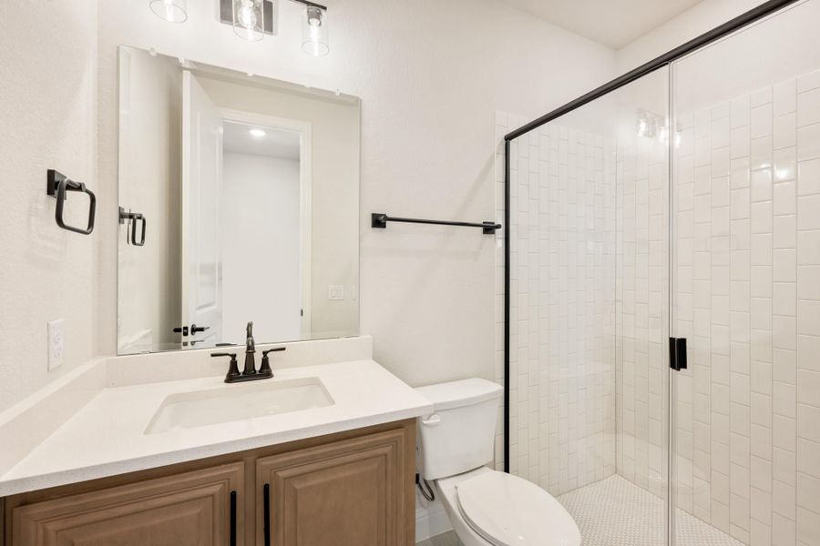 Bathroom with wood vanity, white countertop, and glass-enclosed walk-in shower with white tile Bathroom with wood vanity, white countertop, and glass-enclosed walk-in shower with white tile