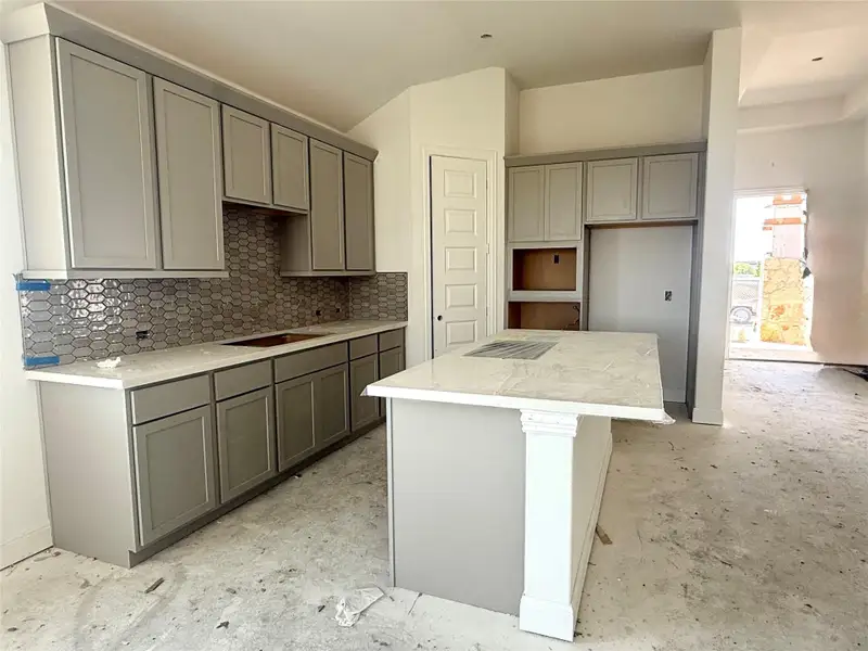 Kitchen featuring gray cabinets, lofted ceiling, a center island, and tasteful backsplash Kitchen featuring gray cabinets, lofted ceiling, a center island, and tasteful backsplash