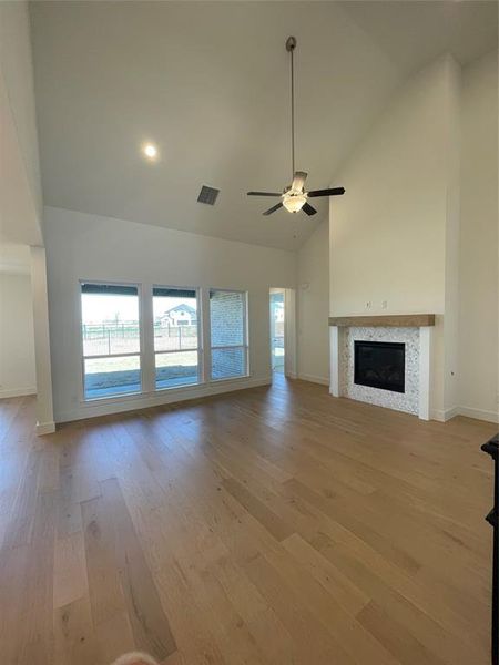 Unfurnished living room with a glass covered fireplace, ceiling fan, lofted ceiling, and light wood-type flooring
