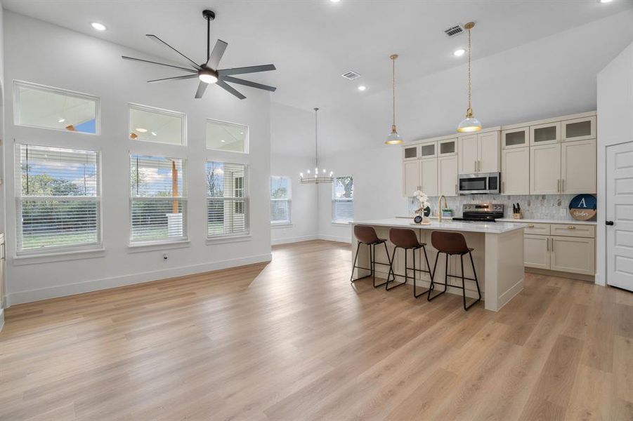 Kitchen featuring tasteful backsplash, a breakfast bar area, a center island with sink, high vaulted ceiling, and glass insert cabinets