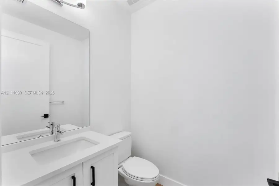 White vanity cabinet with a rectangular basin, quartz countertop, polished chrome faucet, large rectangular mirror, and matte black hardware