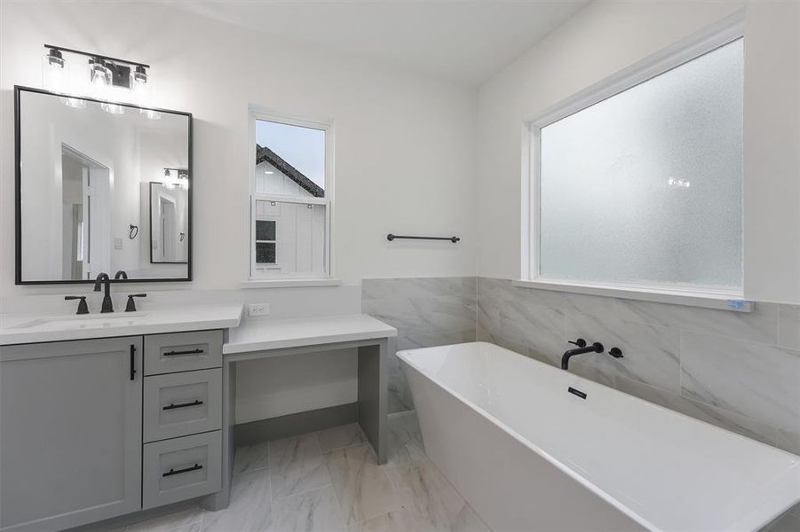 This is a modern primary bathroom featuring a double vanity with framed black matted mirrors, ample storage space and a spacious bathtub with a marble surround. The room is well-lit, with a frosted window ensuring privacy. This bathroom set up is in Plan A only.