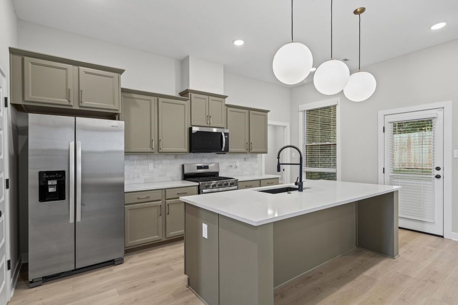 Kitchen featuring appliances with stainless steel finishes, gray cabinetry, decorative backsplash, light wood finished floors, and an island with sink