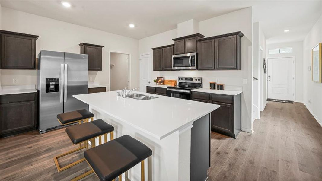 Kitchen with stainless steel appliances, a breakfast bar, dark wood-style flooring, recessed lighting, and an island with sink