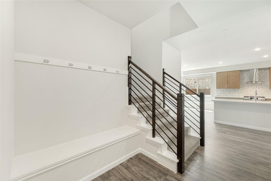Staircase with dark metal railing and white steps, open to kitchen with wood floors throughout