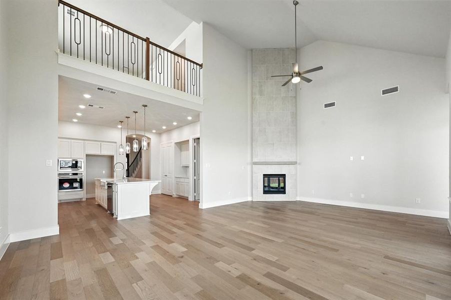 Unfurnished living room with high vaulted ceiling, light wood finished floors, a tiled fireplace, a ceiling fan, and recessed lighting Unfurnished living room with high vaulted ceiling, light wood finished floors, a tiled fireplace, a ceiling fan, and recessed lighting