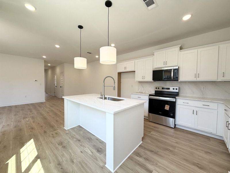 Kitchen featuring stainless steel appliances, an island with sink, light stone countertops, and white cabinetry
