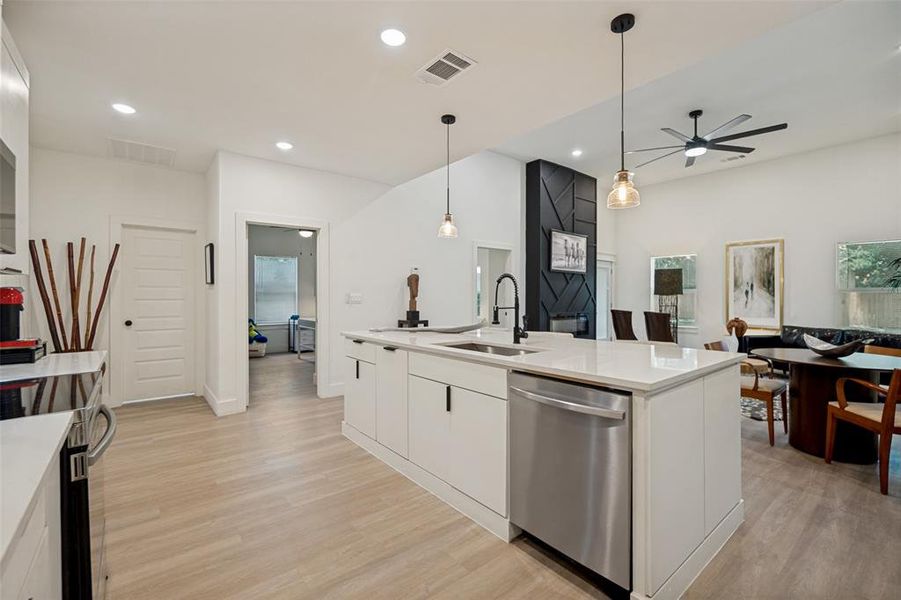 Open-concept kitchen featuring a large island with a stainless steel dishwasher, white countertops, and a black faucet Open-concept kitchen featuring a large island with a stainless steel dishwasher, white countertops, and a black faucet