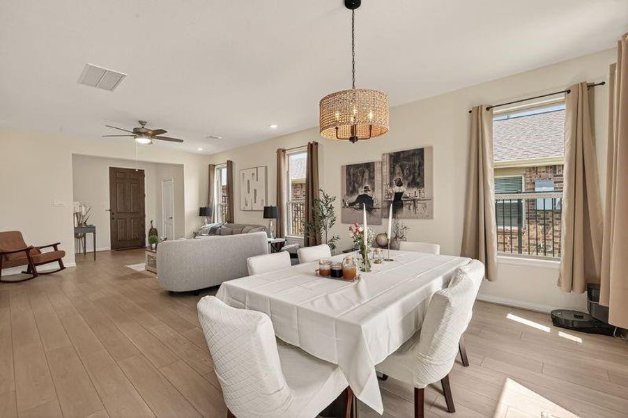 Open-concept dining and living area with light wood floors, oversized windows, and designer lighting.